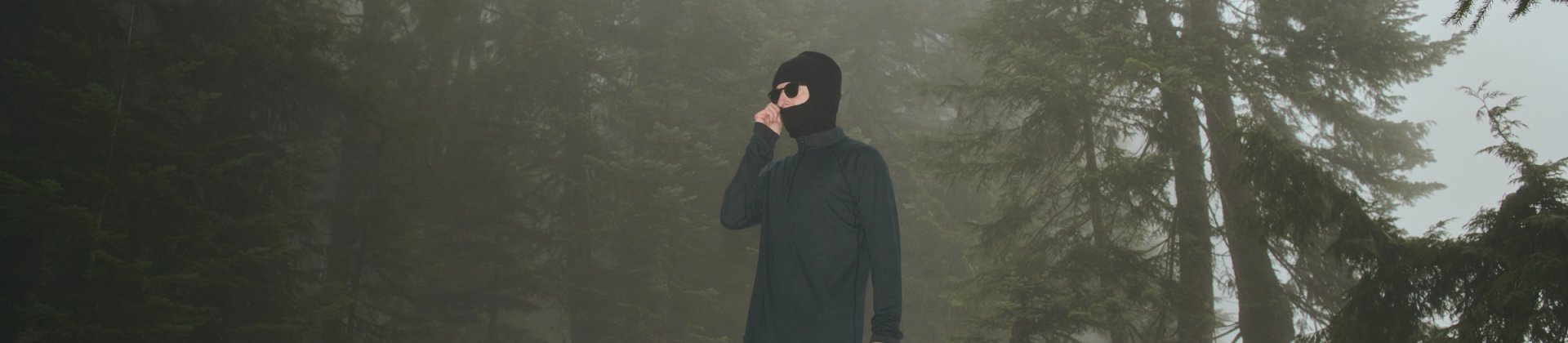 Man outside in forest wearing mid-weight baselayer adjusting ski mask