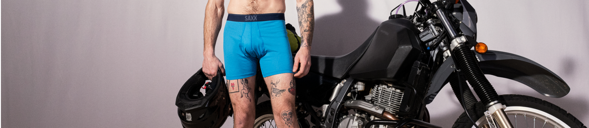 Man in blue Quest underwear standing beside motor bike