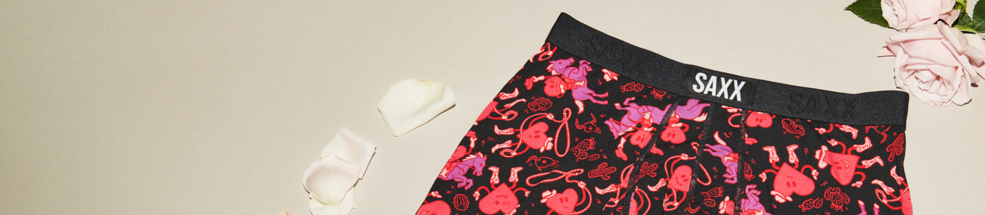 Black underwear with red heart pattern set beside pink rose petals 