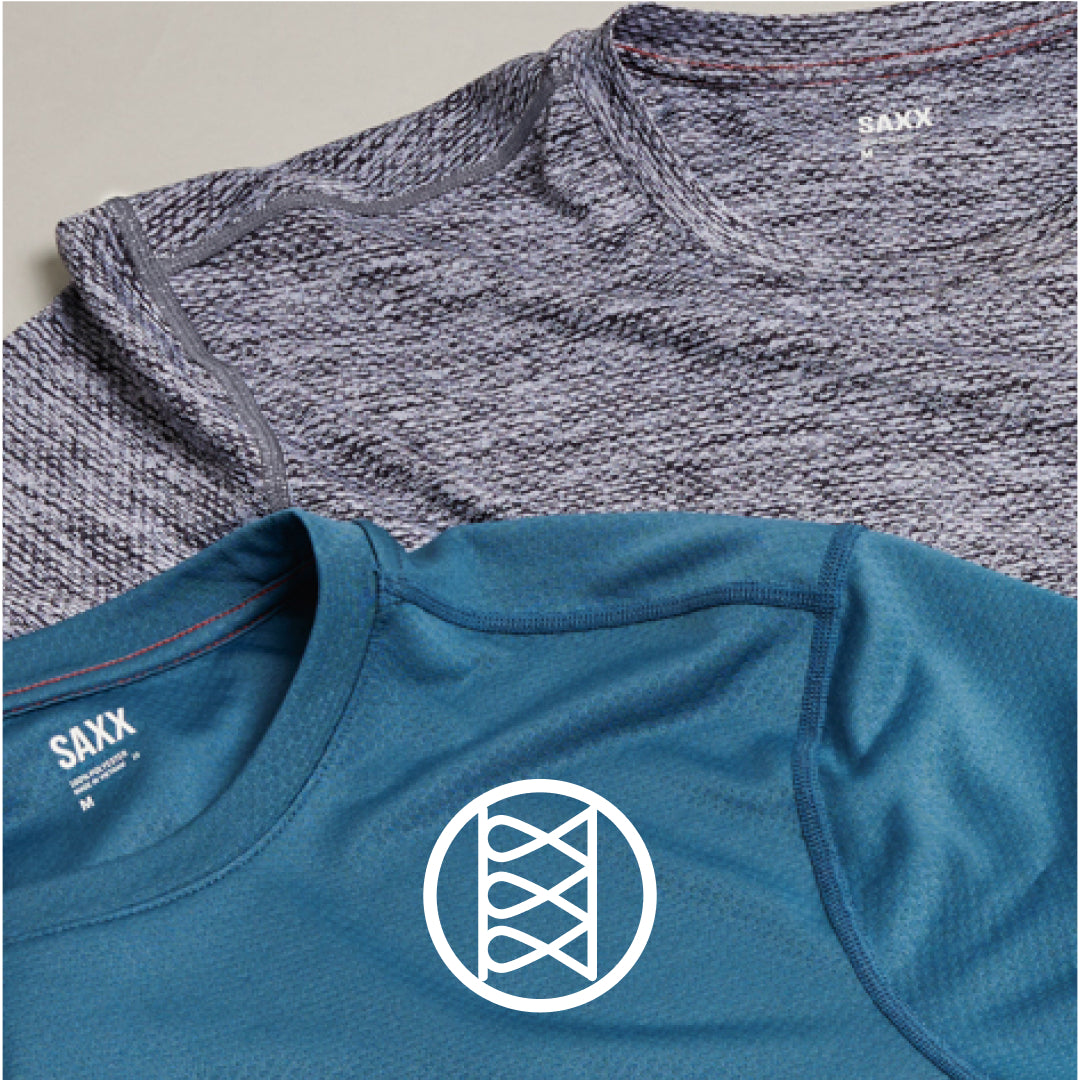 Closeup on two SAXX tees in blue and grey, with a white icon representing chafe-free Flat Out Seams®.