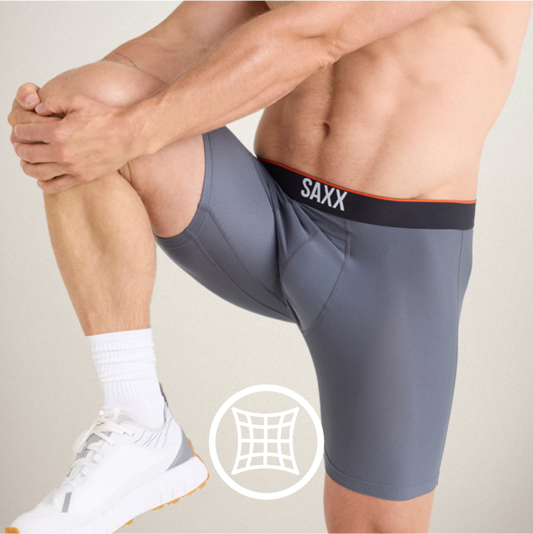 Closeup on man in grey SAXX Performance Boxer Briefs, knee raised in a stretch position. White icon indicates 4-way stretch.