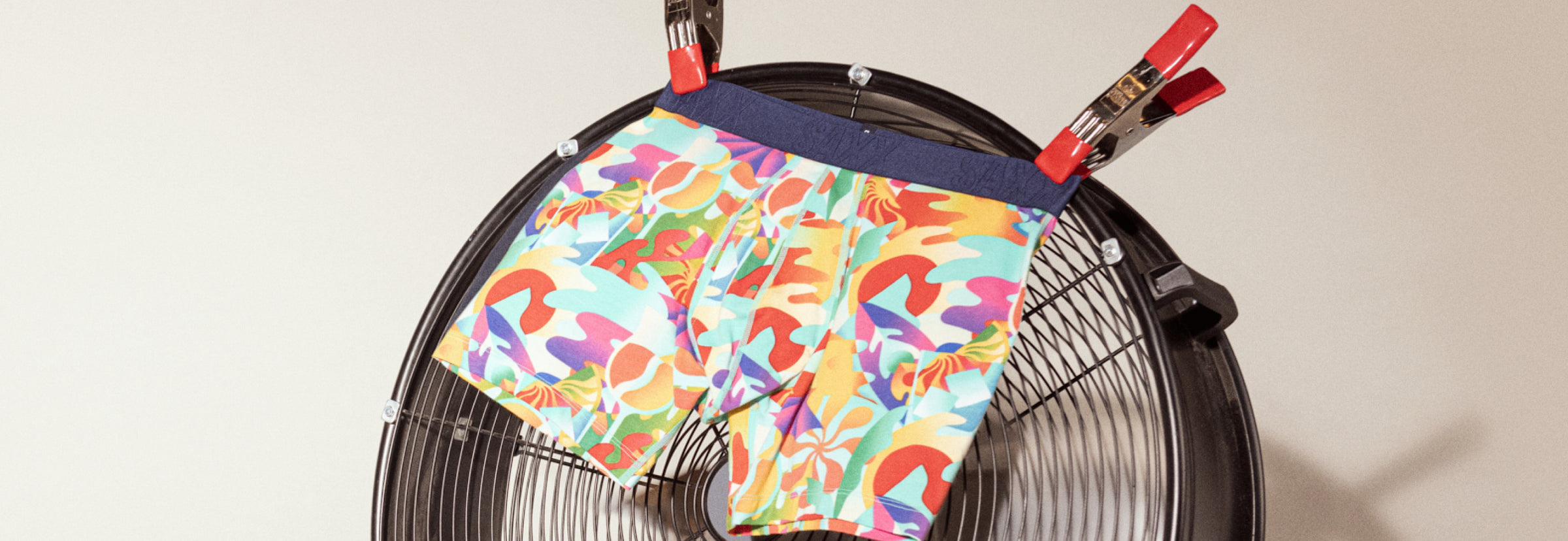 A pair of cooling boxer briefs in a vibrant tropical print clipped to a fan and fluttering