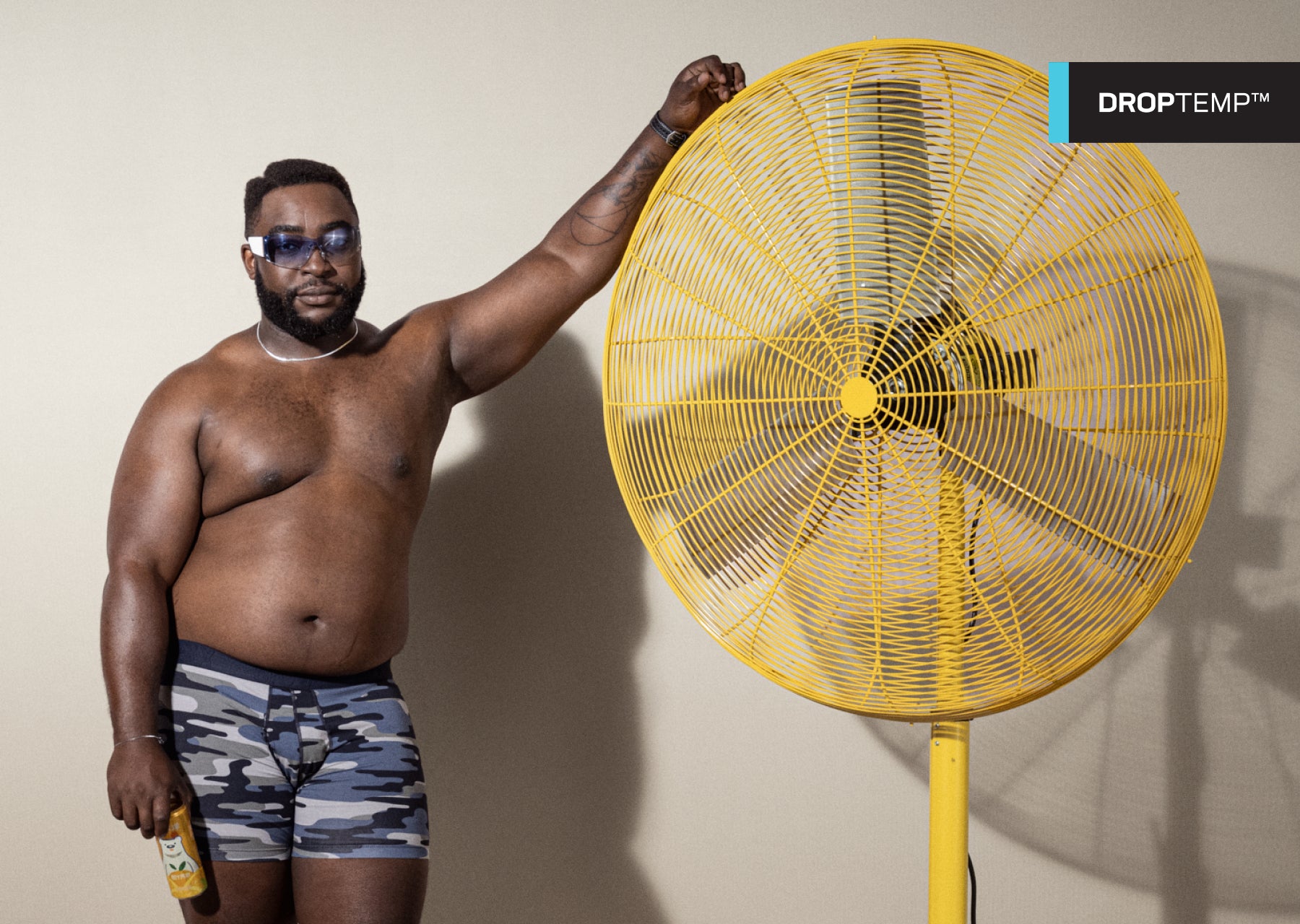 Man wearing sunglasses and blue boxer briefs in camouflage print with his arm propped up on a yellow fan