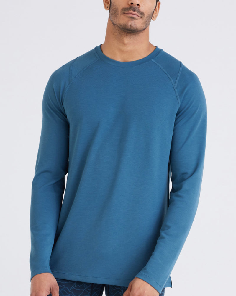 A close up of a man's torso. He is wearing a blue long sleeve t-shirt. He is leaning slightly towards his left.