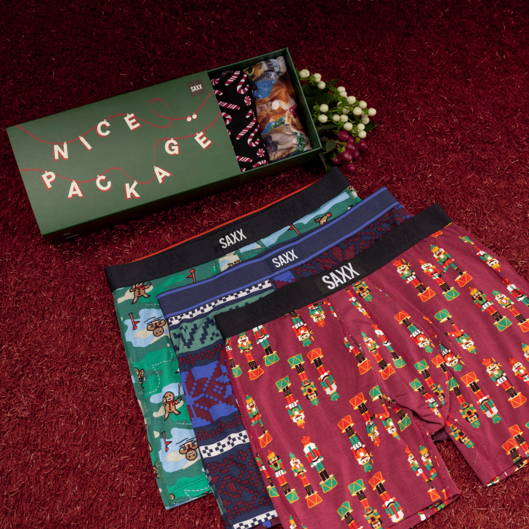 Three pairs of holiday-themed boxer briefs laid on top of each other on a deep maroon carpet. 