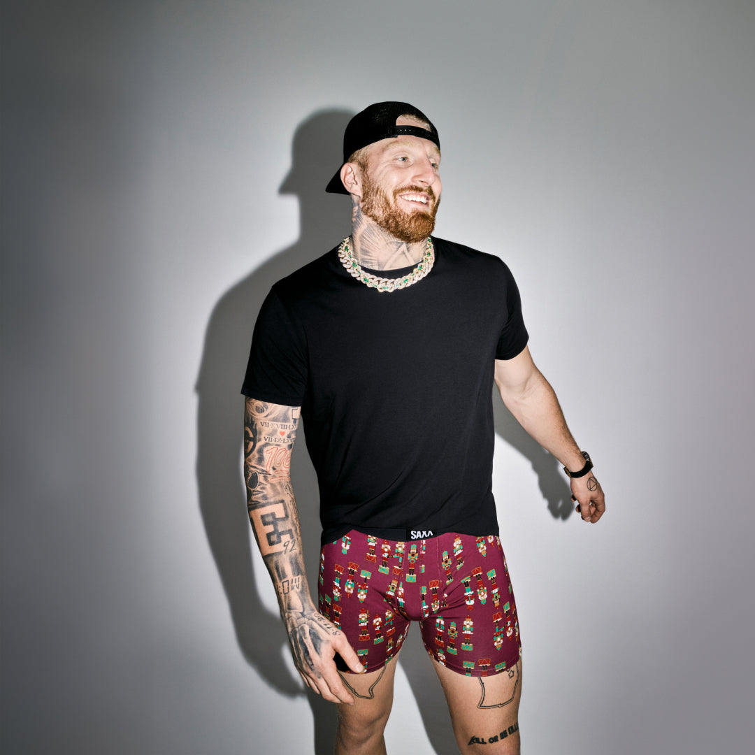 A man wearing a black t-short and holiday printed underwear against a grey background. 