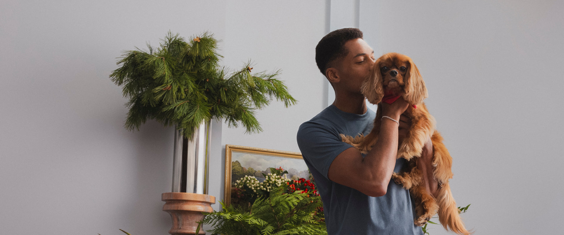 A man holding a dog. The dog wears a Santa Claus hat.