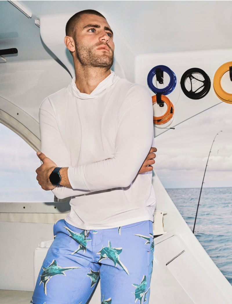 Man on boat wearing blue SAXX 2N1 shorts printed with green marlins, white top, and wristwatch.