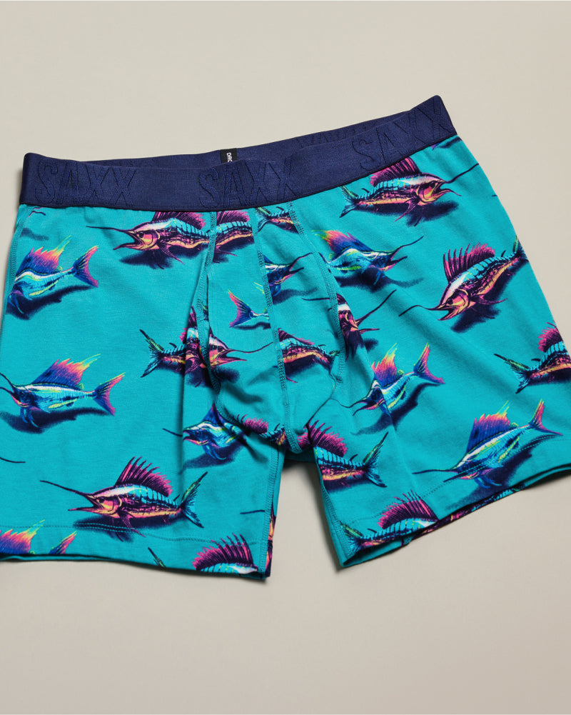 Bright blue SAXX Boxer Briefs with DropTemp® Cooling technology in colorful marlin print laid out flat over neutral background.