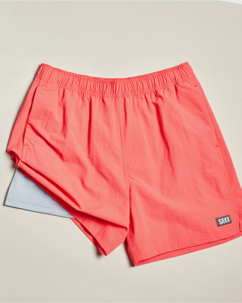 Red SAXX 2N1 Swim Shorts laid out flat over neutral background, one leg lifted to show DropTemp® Cooling Hydro liner.