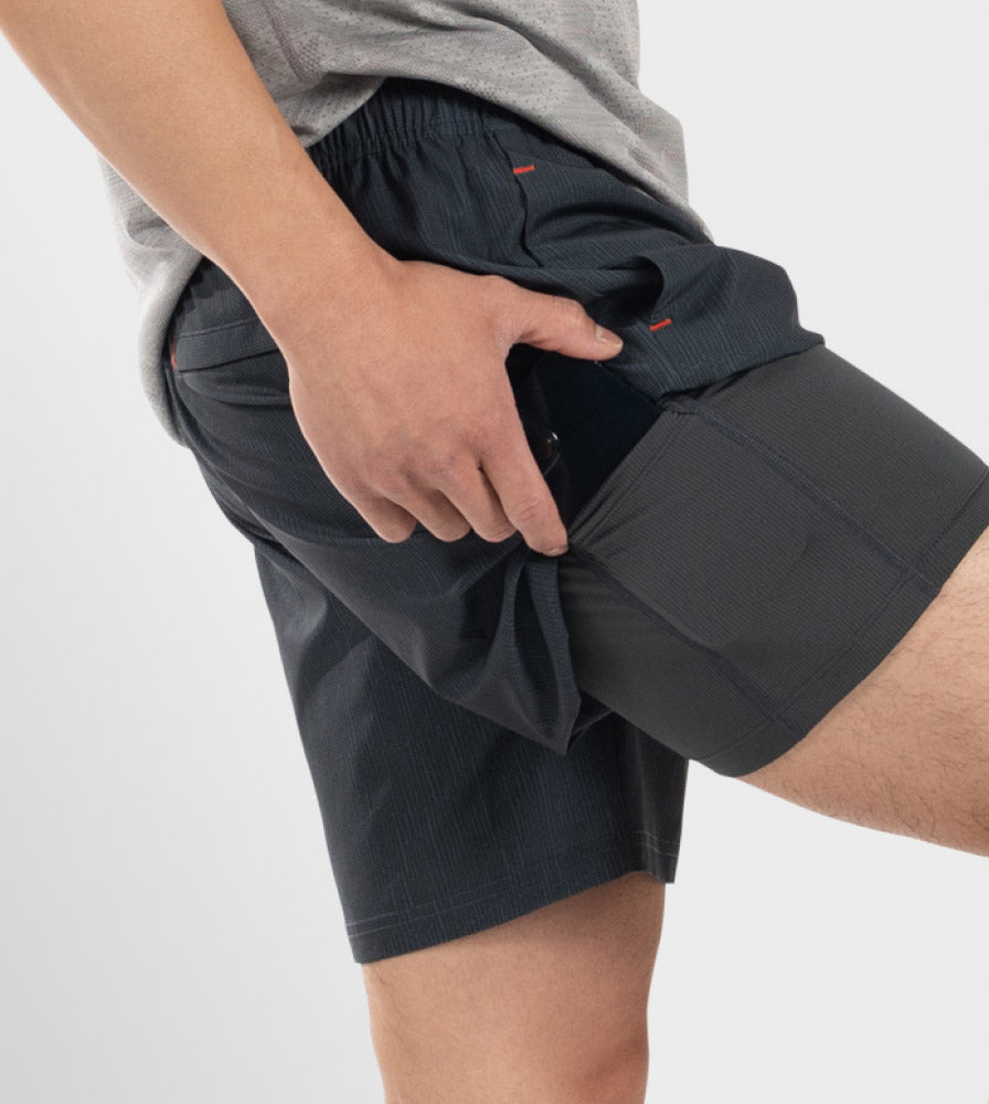 Closeup on side torso of man in black SAXX 2N1 Shorts, lifting leg to place phone in BallPark Pouch® liner.