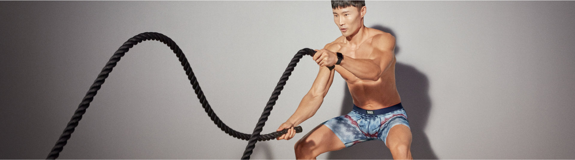 A man squatting and using workout rope wearing patterned boxer briefs. 