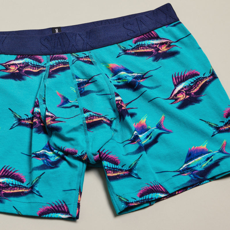 Image of green swordfish printed SAXX Trunks and a folded multi-colored pair on a neutral backdrop.