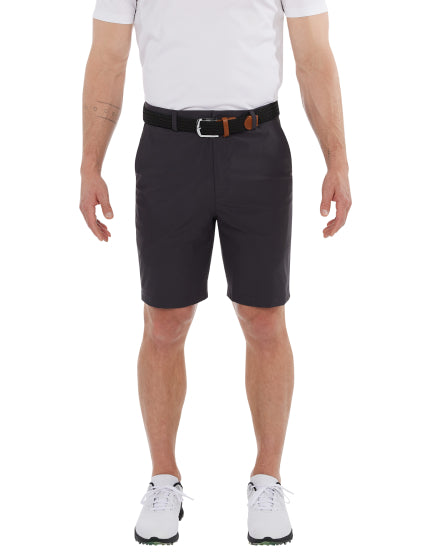 Man wearing navy SAXX Caddie Shorts, white tee, white sneakers, and black belt, standing against white backdrop.