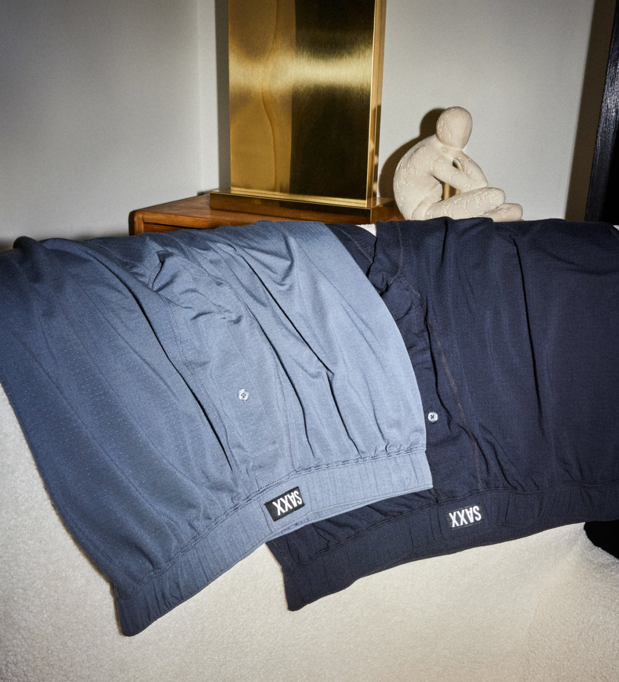 Two pairs of blue pyjama bottoms hanging over a surface with their waistbands and button flies shown. 