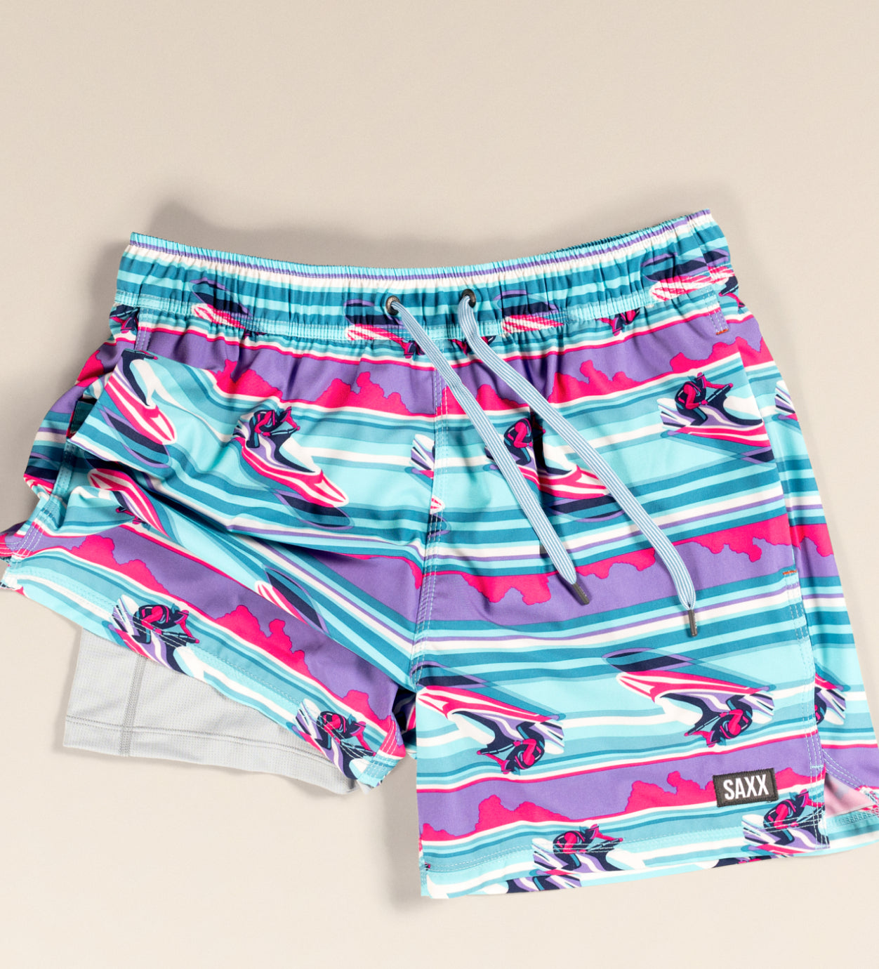 A pair of brightly patterned swim shorts laid flat with the right leg ruched up to reveal a mesh liner.