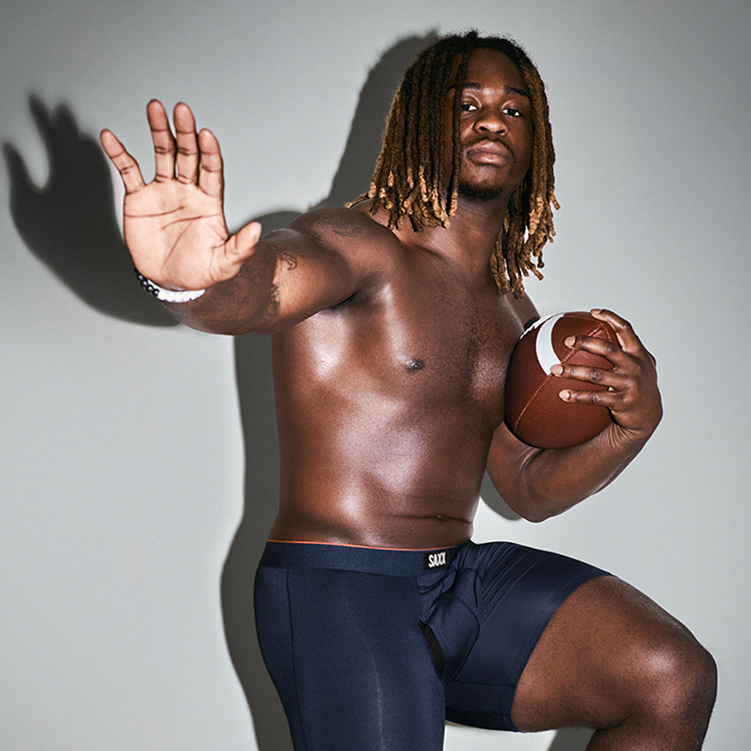 SAXX Gamechanger and College Football player Ashton Jeanty holds a football while wearing only the Multi-Sport Mesh Boxer Brief.
