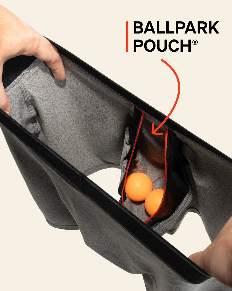 Men’s hands holding a pair of grey SAXX Boxer Briefs open from the waistband, revealing the built-in BallPark Pouch®.