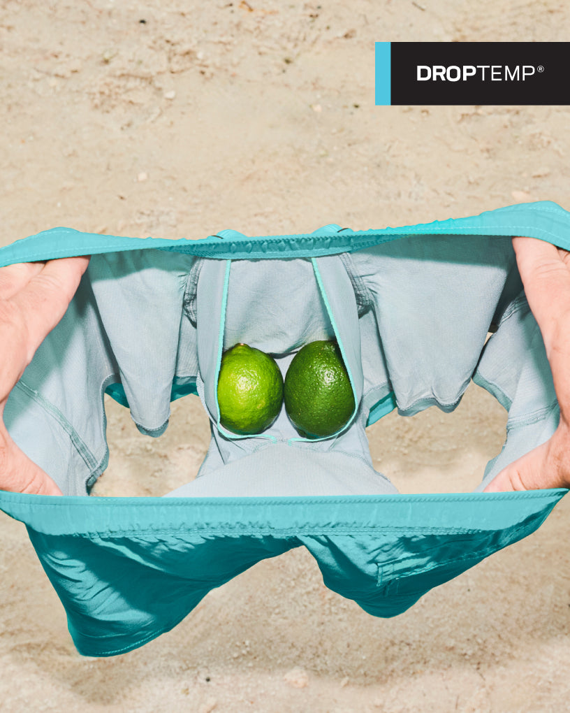 A pair of SAXX 2N1 shorts being held open by a pair of hands showcasing a pair of limes sitting in the BallPark Pouch®.