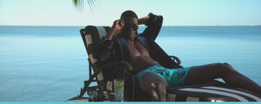 A man relaxing by the ocean wearing a navy robe and brightly printed boxer briefs.