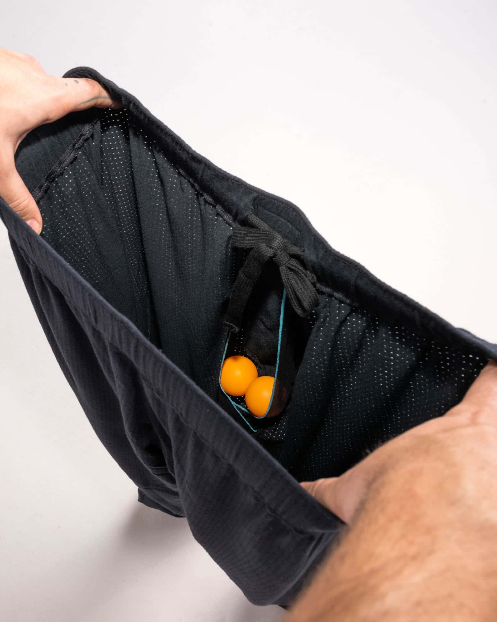 Man's hands revealing inside of 2N1 shorts showing liner with pouch holding two ping pong balls