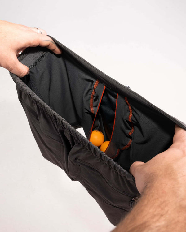 Man's hands revealing inside of 2N1 shorts showing liner with pouch holding two ping pong balls