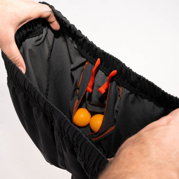 Man's hands revealing inside of 2N1 shorts showing liner with pouch holding two ping pong balls