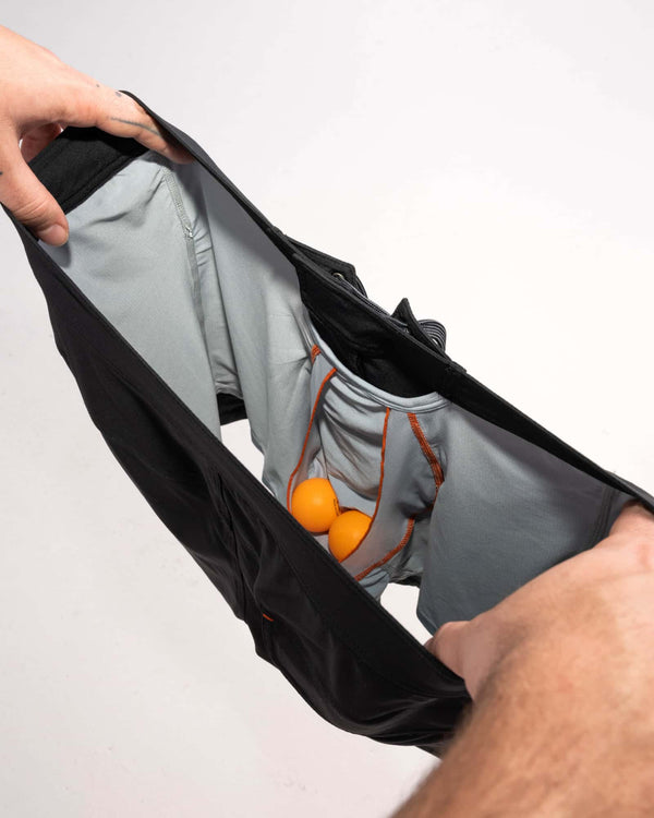 Man's hands revealing inside of 2N1 shorts showing liner with pouch holding two ping pong balls